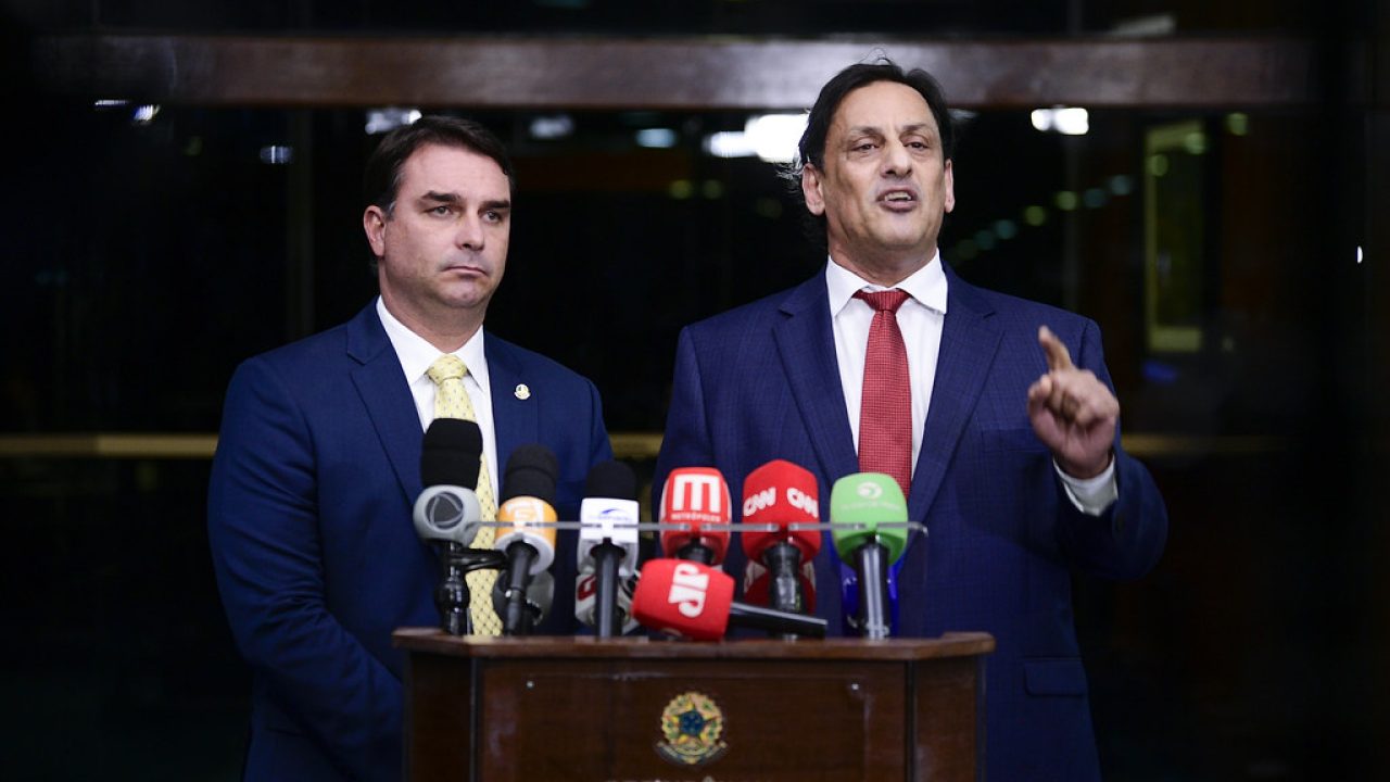 Candidato Flávio Bolsonaro em evento de campanha, ao lado de Lula em discurso, ambos em propaganda eleitoral na TV