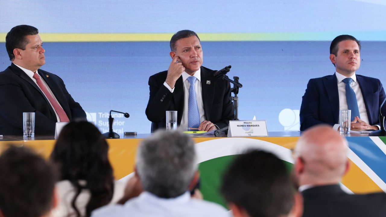Placas de urna e tela de resultados do TSE mostrando a apuração das Eleições 2026