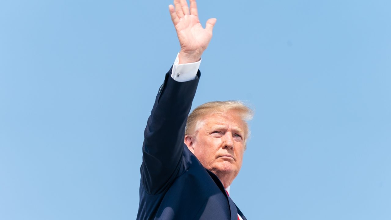 Donald Trump falando em evento, com fundo de bandeira dos EUA